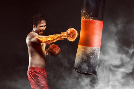 Asian athlete boxer punching a punching bag with effect dramatic lighting in studioの写真素材