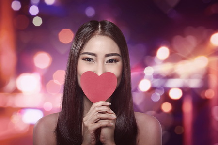 Beautiful asian woman holding a red heart shape in front of her faceの写真素材