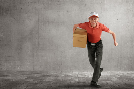 Asian delivery courier holding package running over gray backgroundの写真素材