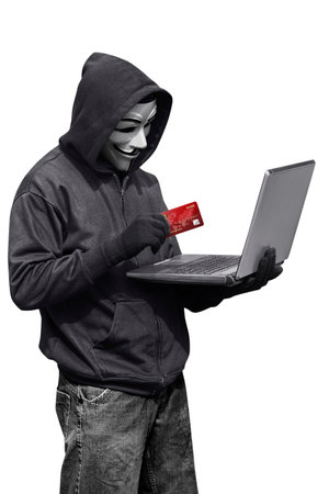 Hacker man wearing anonymous mask holding laptop and credit card while standing isolated against white backgroundのeditorial素材
