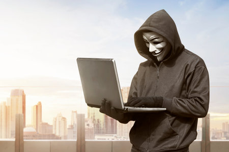 Hacker man with anonymous mask using laptop to hacking in the modern buildingのeditorial素材