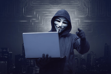 Hacker man with mask holding laptop while appoint against virtual backgroundのeditorial素材