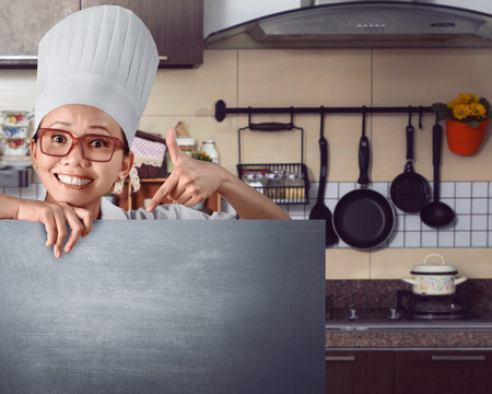 Happy asian chef showing menu sign on chalkboard against kitchen backgroundの写真素材