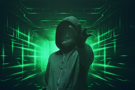 Hooded hacker with mask grabbing something against green visual backgroundの写真素材