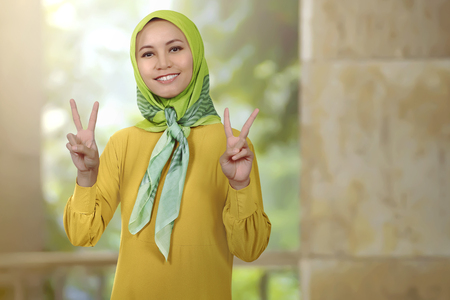 Smiling asian woman girl with hijab showing peace sign in the mosqueの写真素材
