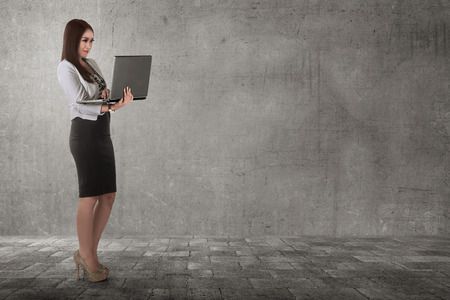 Smiling asian business woman typing while holding laptop in the streetの写真素材