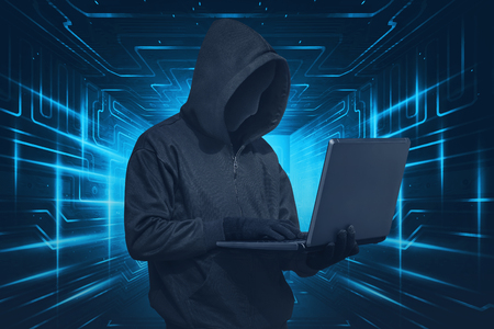 Hacker man with mask using laptop while standing against digital backgroundの写真素材