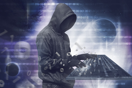 Hooded hacker man with anonymous mask typing on virtual keyboard over binary code backgroundの写真素材