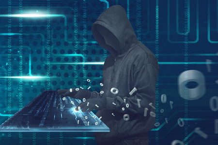 Hooded man with anonymous mask typing on virtual keyboard over binary code backgroundの写真素材