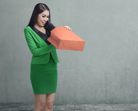 Happy asian business woman opening her shopping bag against street wall backgroundの写真素材