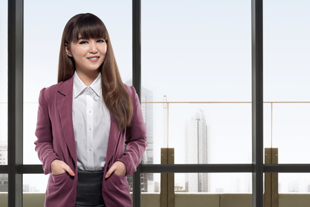 Smiling asian business woman standing in front of windows in an officeの写真素材