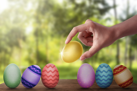 Hand put gold easter egg in row on wooden plank against blurred backgroundの写真素材