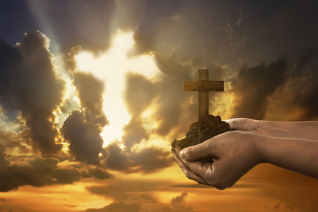 Human hand holding christian cross with soil on the hand under sunset backgroundの写真素材