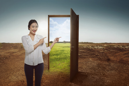 Beautiful asian business woman showing green meadow panorama from the open door over cracked land backgroundの写真素材