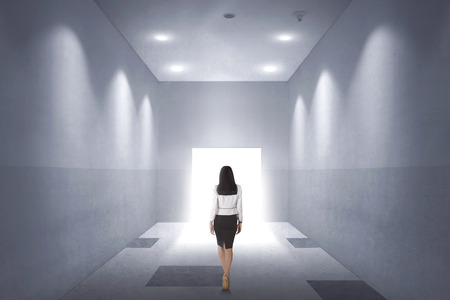Back view of a young asian business woman walking to opened door in the officeの写真素材