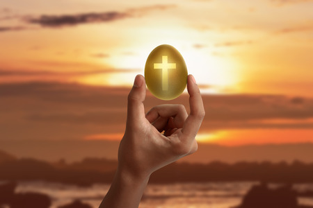 Hand holding the light of cross shape from the golden egg at sunsetの写真素材
