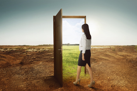 Young asian business woman walking to the open door going to green environment on cracked land backgroundの写真素材