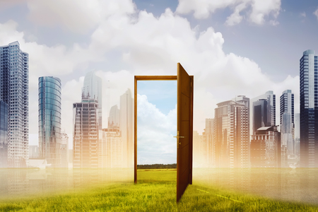 Open wooden door to the new world with green meadow against cityscape backgroundの写真素材