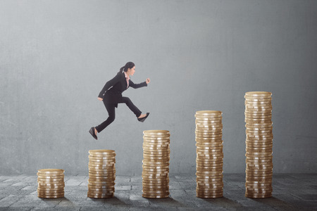 Young asian business woman climb up the gold coins on a grey backgroundの写真素材