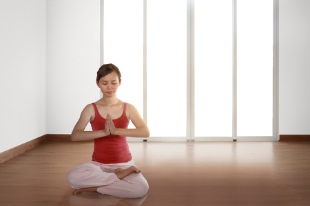 Young asian woman doing yoga in a lotus position at homeの写真素材