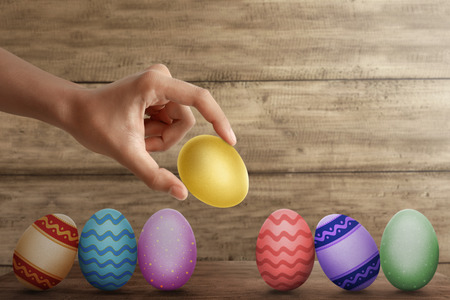 Hand put gold easter egg in row on desk with wooden wall backgroundの写真素材