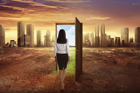 Asian business woman walking to the open wooden door with green environment leaving modern cityの写真素材