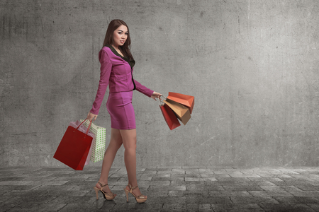 Portrait of asian business woman with shopping bags walking in the street against grey wall backgroundの写真素材