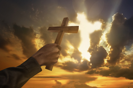 Man hand holding wood cross or religion symbol shape over a sunset sky with clouds backgroundの写真素材