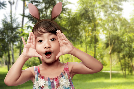 Cute little asian girl wearing bunny ears on Easter day on the fieldの写真素材