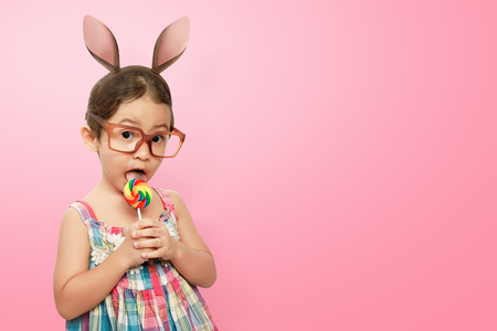 Smiling asian child girl wearing bunny ears on Easter day against pink backgroundの写真素材