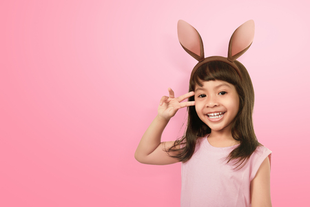 Fun asian little girl wearing bunny ears on Easter day against pink backgroundの写真素材