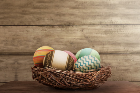 Colorful easter eggs in basket on wooden backgroundの写真素材