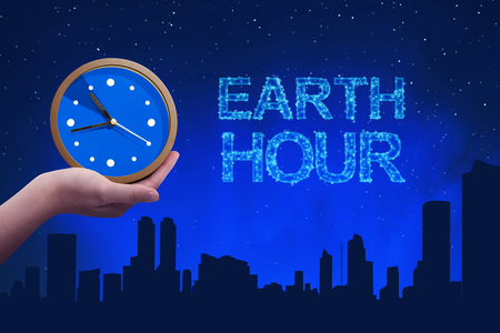 People hand holding a clock with earth hour greeting against a background night sceneの写真素材
