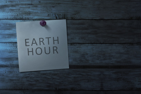 Hanging note paper with earth hour message on wooden wall at dark room backgroundの写真素材