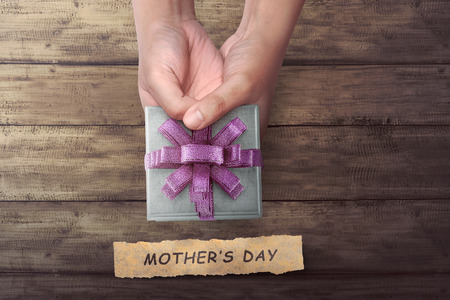 People hand holding small gift with Mother's Day greeting on wooden tableの写真素材