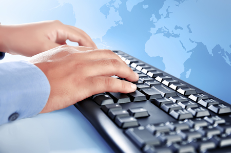 Businessman hand typing on keyboard against blue globe backgroundの写真素材