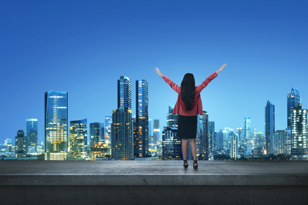 Happy asian business woman standing on a edge a rooftop at nightの写真素材