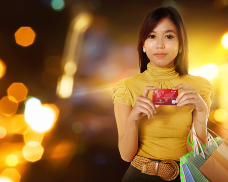 Beautiful asian woman with shopping bags and credit card in the hands over blurred backgroundの写真素材