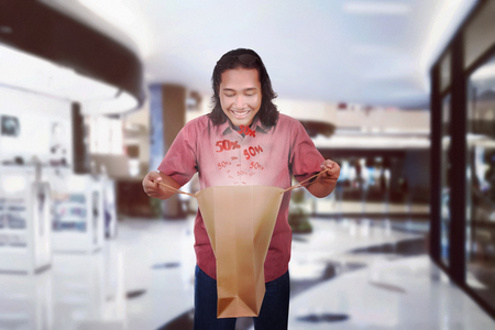 Image of shocking long haired man open shopping bagの写真素材
