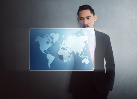 Modern asian businessman touching virtual world map on digital screen over wall backgroundの写真素材
