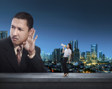 Business woman communicate with her partner using megaphone against city night backgroundの写真素材