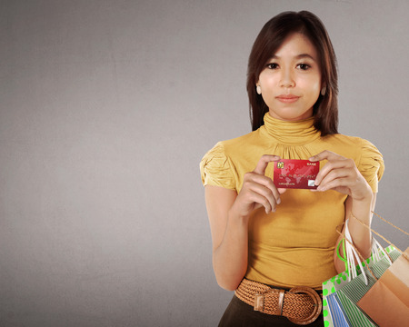 Happy asian woman with many shopping bags and credit card in her hand against grey backgroundの写真素材