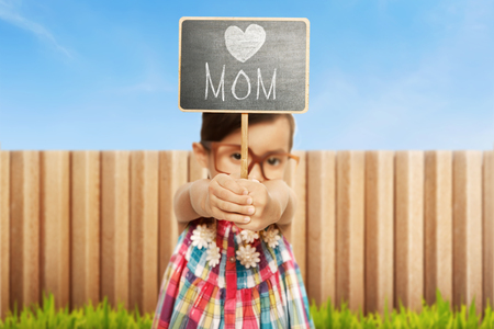 Asian little girl holding chalkboard with Happy mothers day message on green grassの写真素材