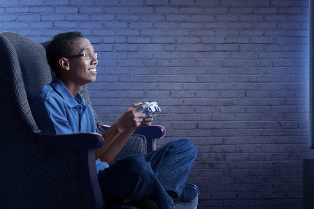Happy asian nerd man in sofa with gamepad playing game at homeの写真素材