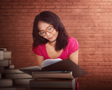 Portrait of a serious young asian woman reading a book in a libraryの写真素材