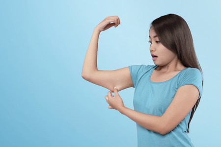 Young asian woman losing muscle on her arm on blue backgroundの写真素材