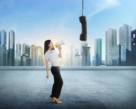Beautiful asian business woman with bullhorn screaming to receiver on outside buildingの写真素材