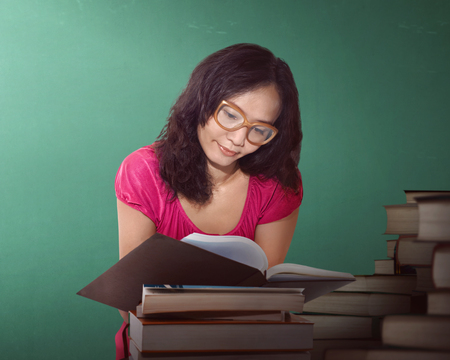 Asian woman reading a book at a library with green backgroundの写真素材