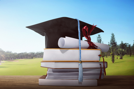 Mortarboard and graduation scroll with stack of book on wooden tableの写真素材