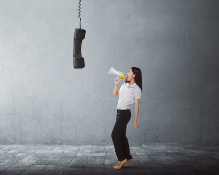Young asian business woman screaming using a megaphone to black receiver in the city streetの写真素材